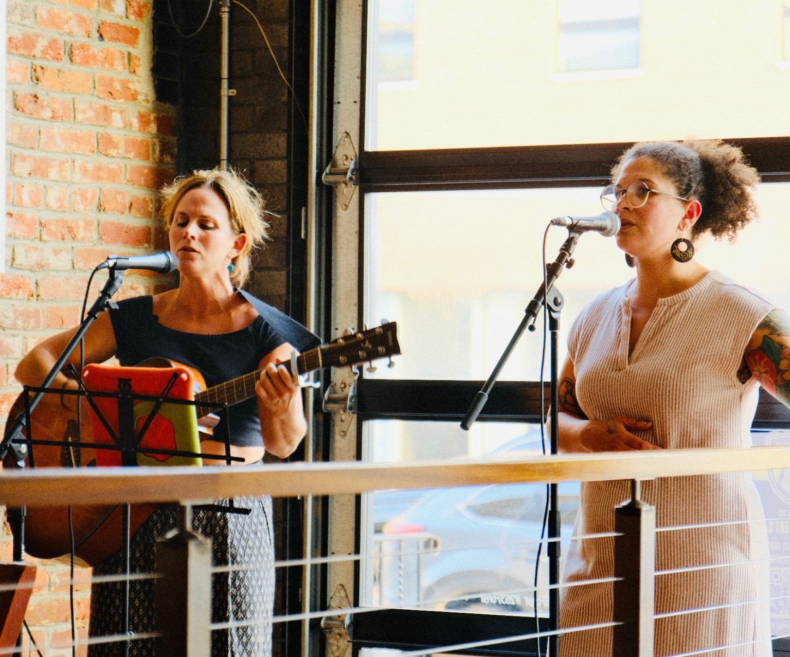 Katie singing and playing acoustic guitar alongside Zena at a live show